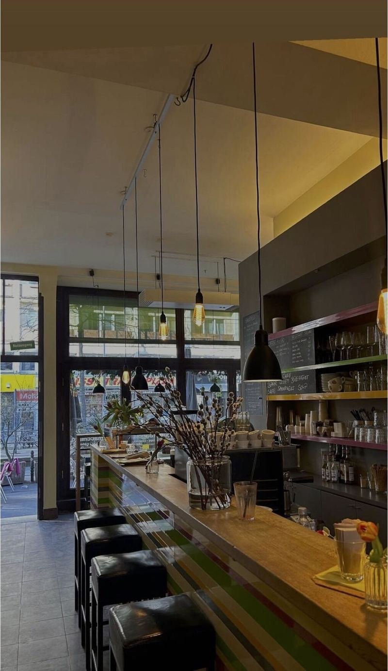 Blick über die lange gestreifte Theke zur Kaffeemaschine, dahinter das hohe Fenster