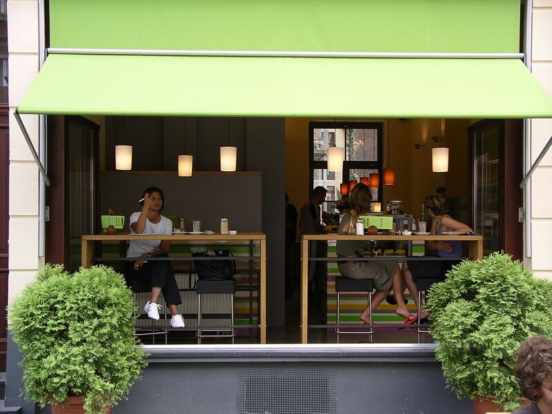 Der offene Eingang des cafecafe an der Aachener Straße mit grüner Markise