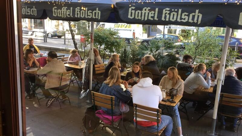 Gut besetzte Terrasse des cafecafe unter Sonnenschirmen an der Aachener Straße