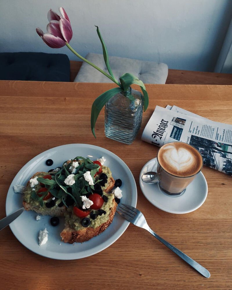 Avocado-Brot mit Feta und ein Cappuccino auf einem Holztisch